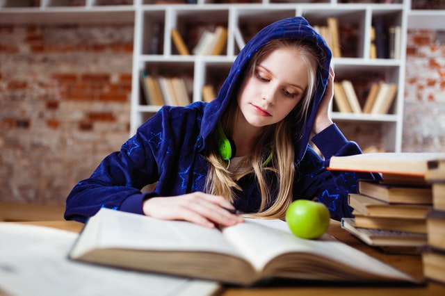 teen sitting indoors reading with apple on desk