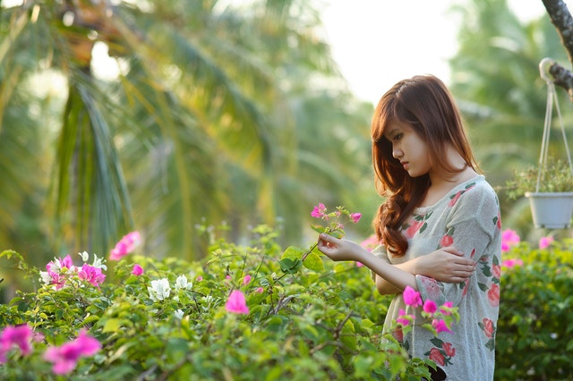 young woman standing in a garden holding a flower