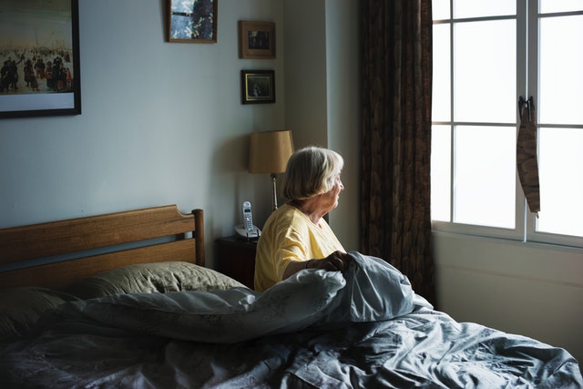 elderly woman on bed looking out towards window