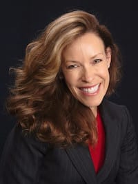 Therapist Stephanie Roberts headshot indoors in front of a black background wearing a black blazer and red top