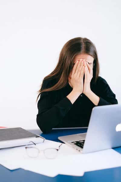 woman sitting in front of computer covering face with her hands
