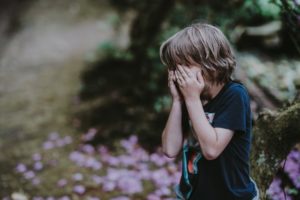 child standing outdoors covering eyes